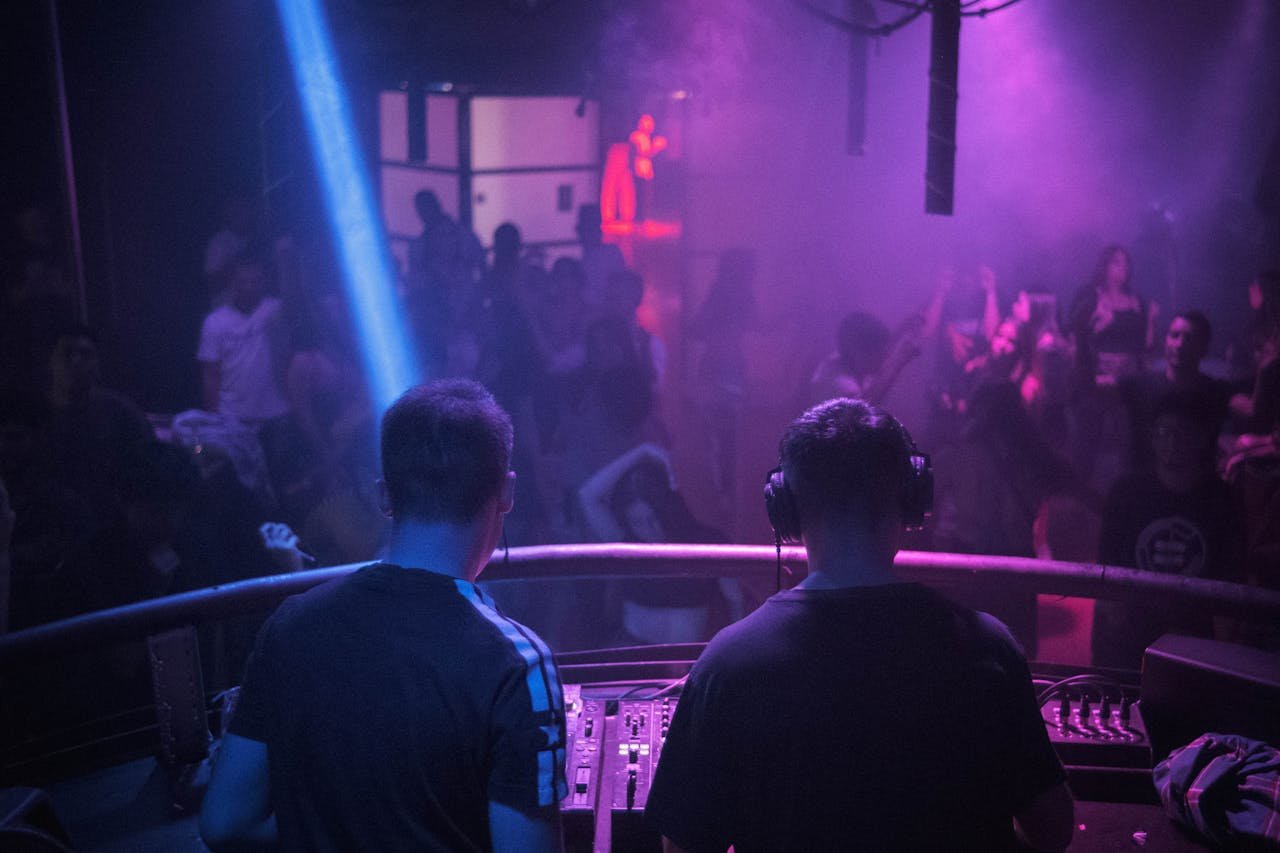 classes-04 A lively night club scene with a DJ mixing music amidst vibrant lights and dancing crowd.