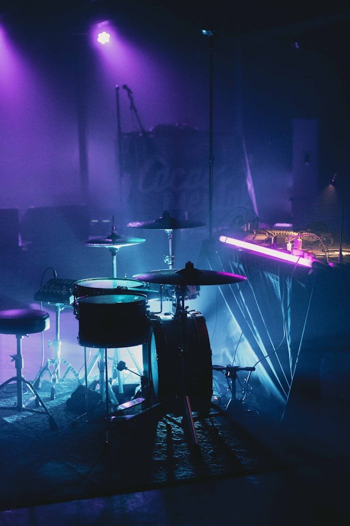 Drum set on a dimly lit stage with vibrant purple lighting, creating a dramatic concert atmosphere.