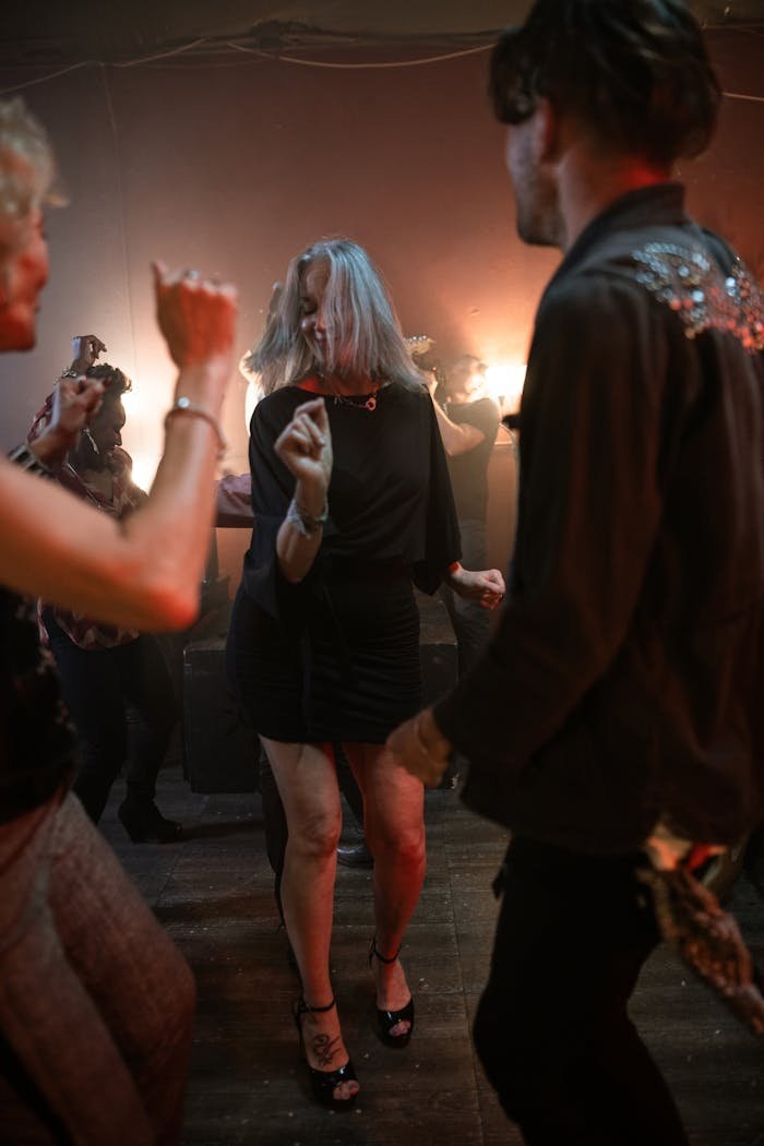 gallery-7 A lively group of adults dancing energetically at a nightclub party under warm lights.